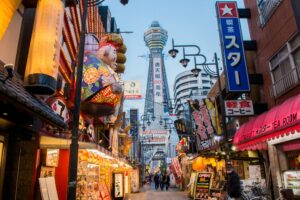 Torre Tsūtenkaku vista dalla via del quartiere Shinsekai con insegne luminose, Osaka, Giappone