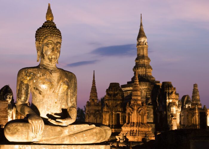 Statua del Buddha e rovine del tempio illuminate al crepuscolo nel Parco Storico di Sukhothai, Thailandia