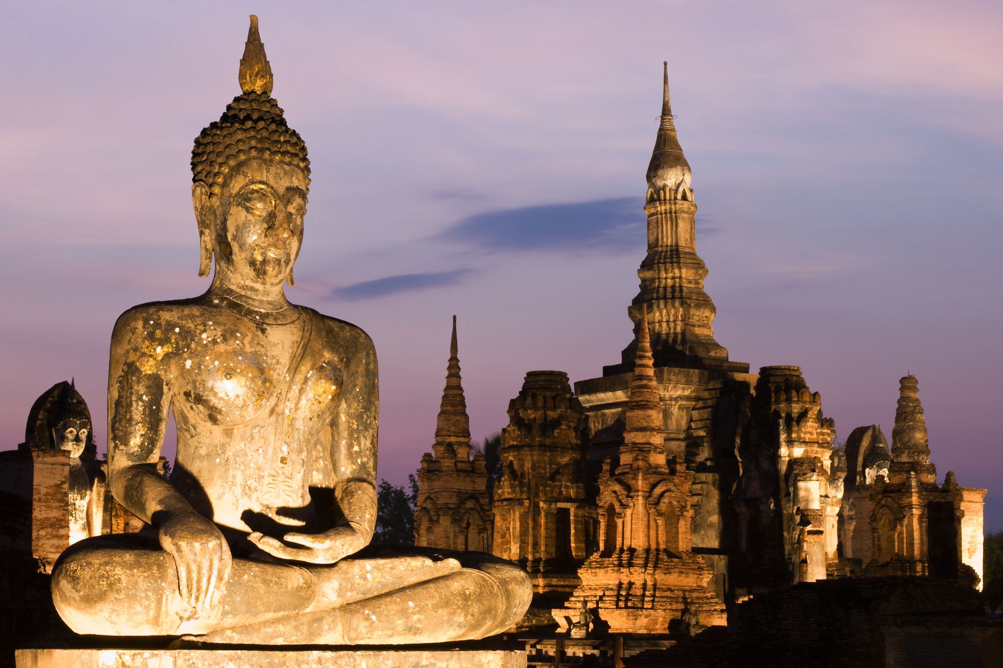 Statua del Buddha e rovine del tempio illuminate al crepuscolo nel Parco Storico di Sukhothai, Thailandia